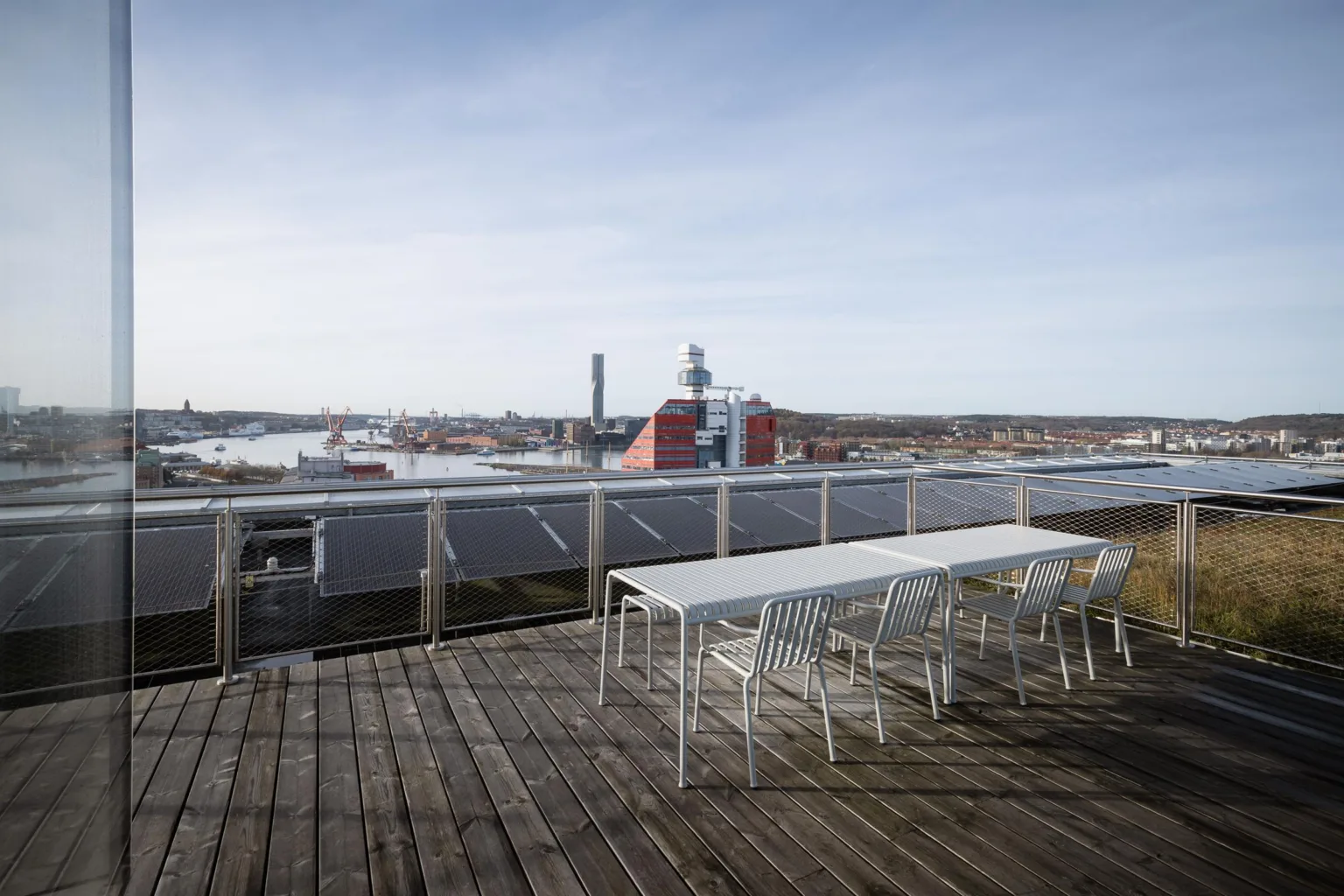 En takterrass med trämöbler och utsikt över en stad med industriella byggnader och vatten.