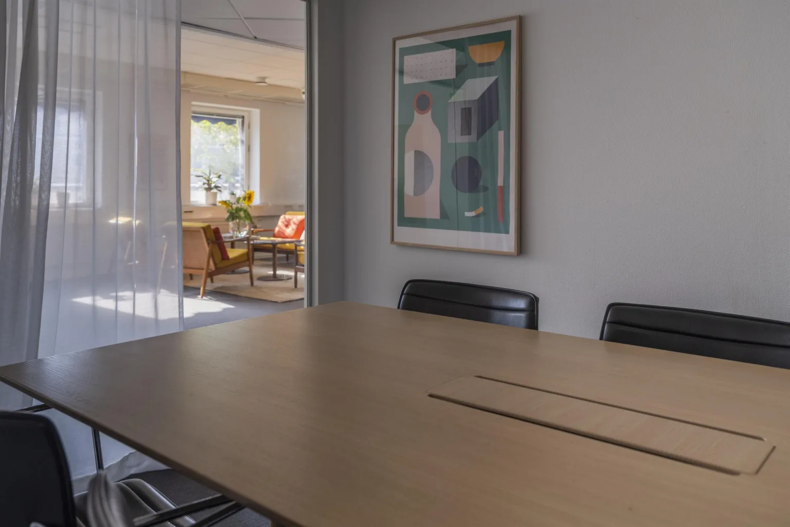 Ett konferensrum med ett bord, stolar och en tavla på väggen, med utsikt mot en ljusare del av kontoret.