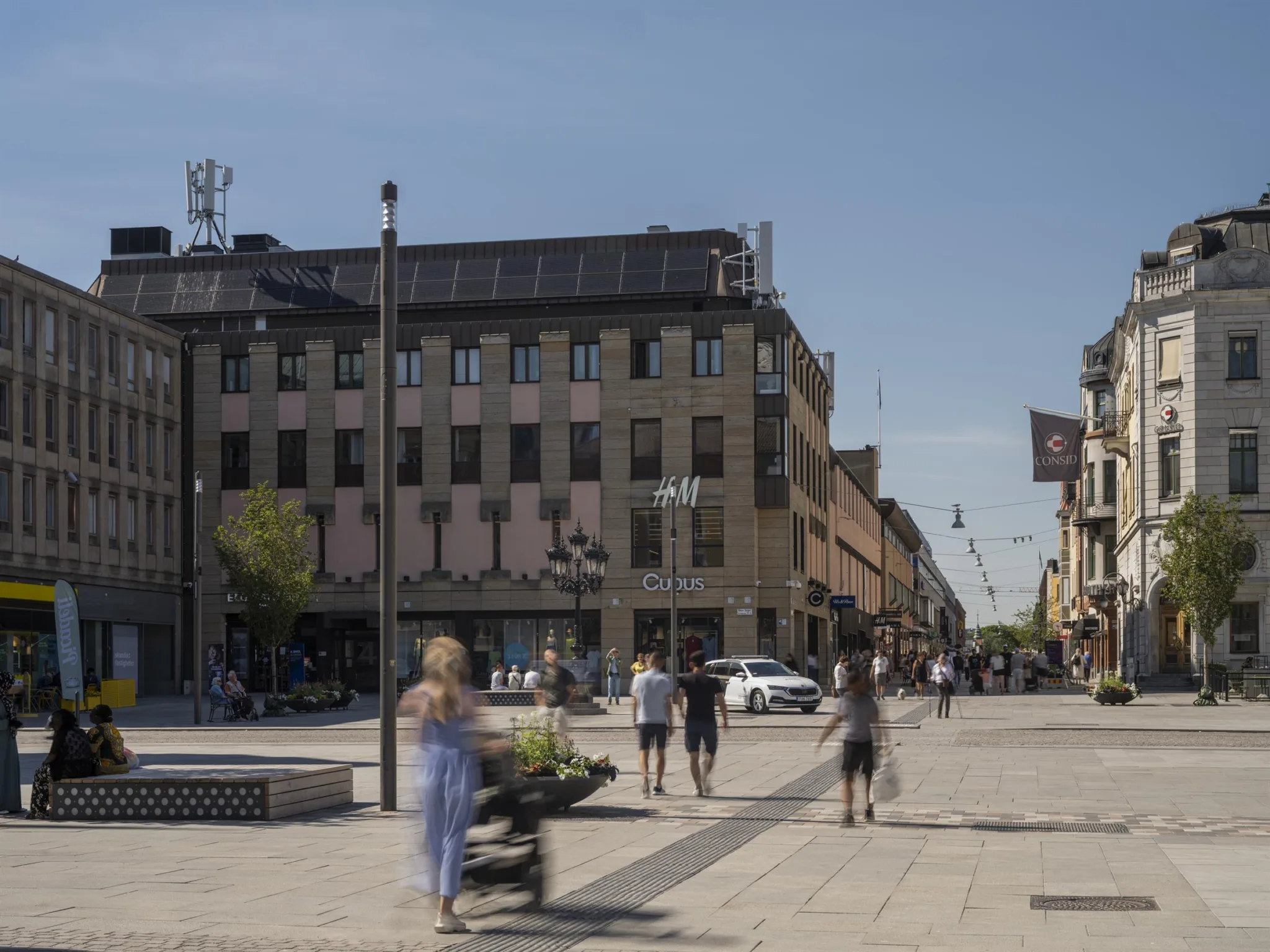 En stadsgata med fotgängare, byggnader och klar blå himmel.