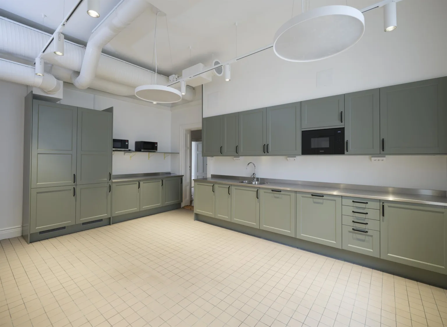 Ett stort kök med gråa skåp, beige golv och modern inredning, inklusive en inbyggd mikrovågsugn.