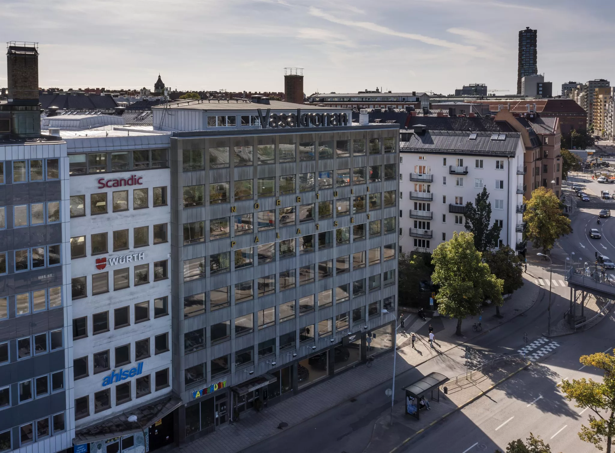 En modern kontorsbyggnad med glasfasad, omgiven av gator och andra byggnader i stadsmiljö.