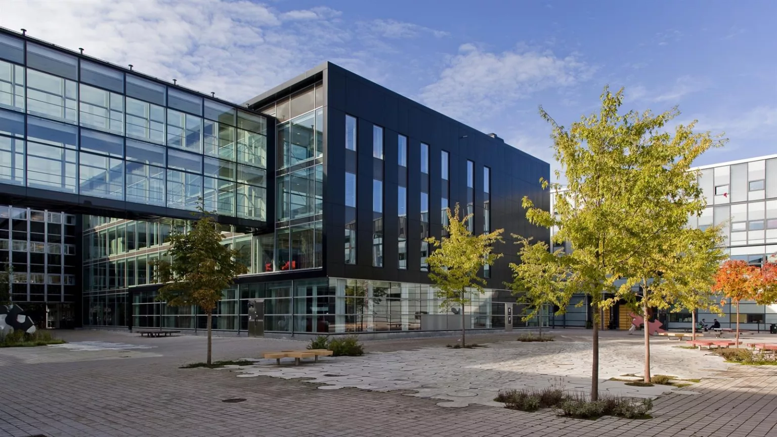 5. En svart och glasbeklädd modern byggnad med träd och stenlagd gårdsplan.