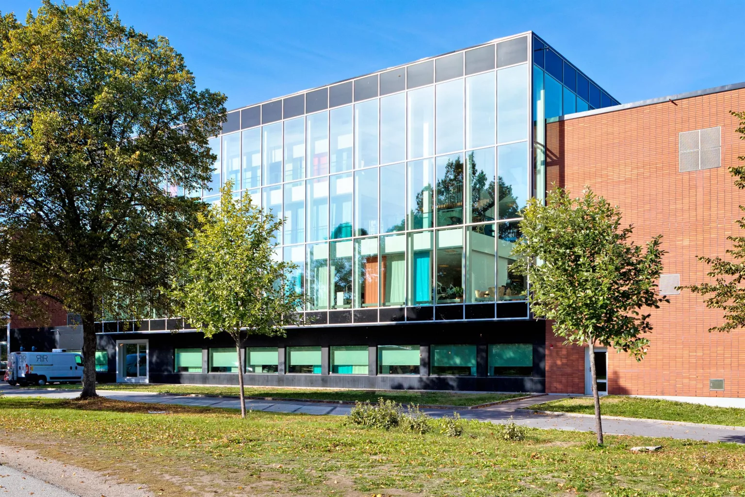 1. En modern byggnad med glasfasad och tegelvägg, omgiven av grönska och träd.