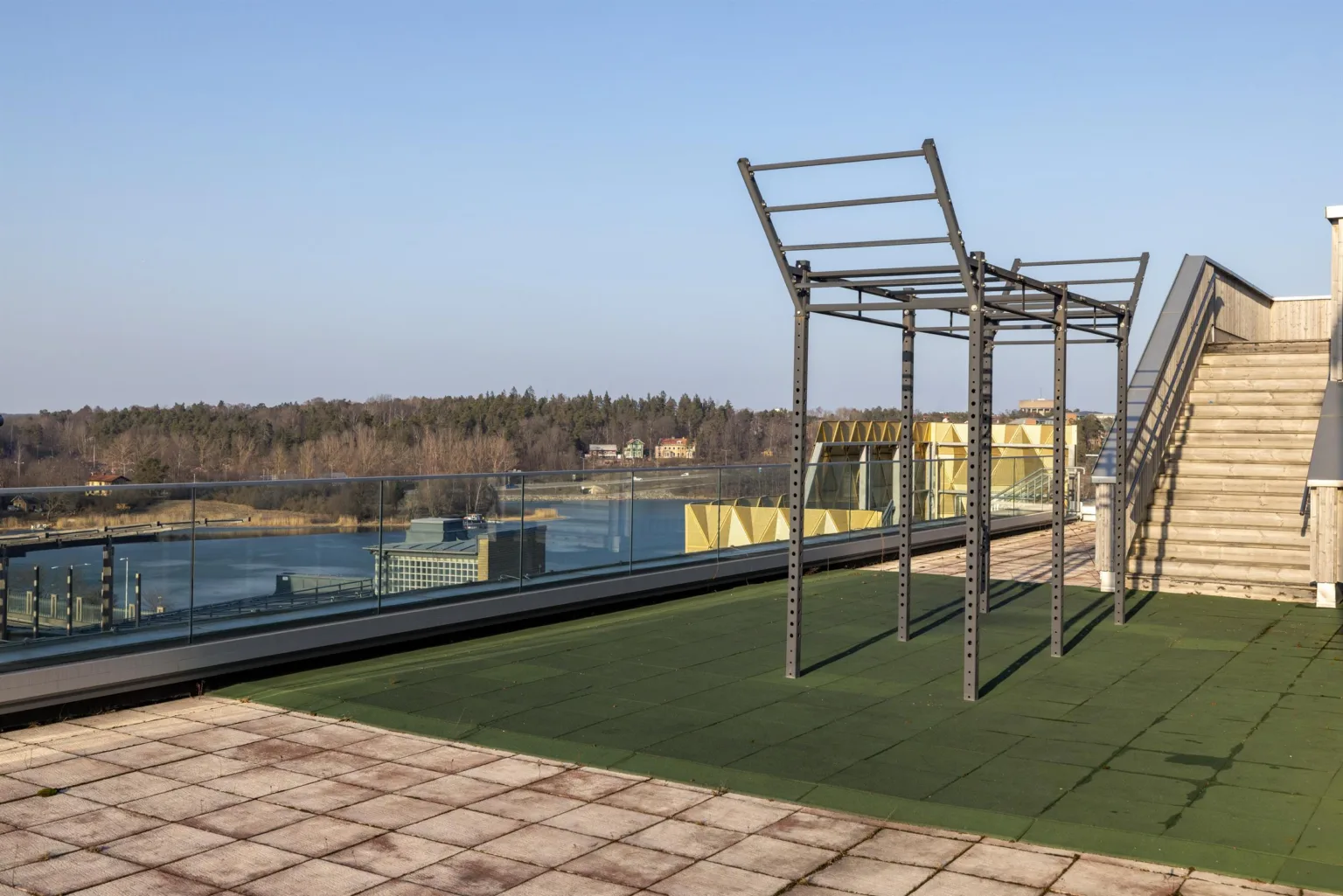 En träningsyta utomhus med metallställningar på konstgräs, omgiven av en sjö och skog i bakgrunden.
