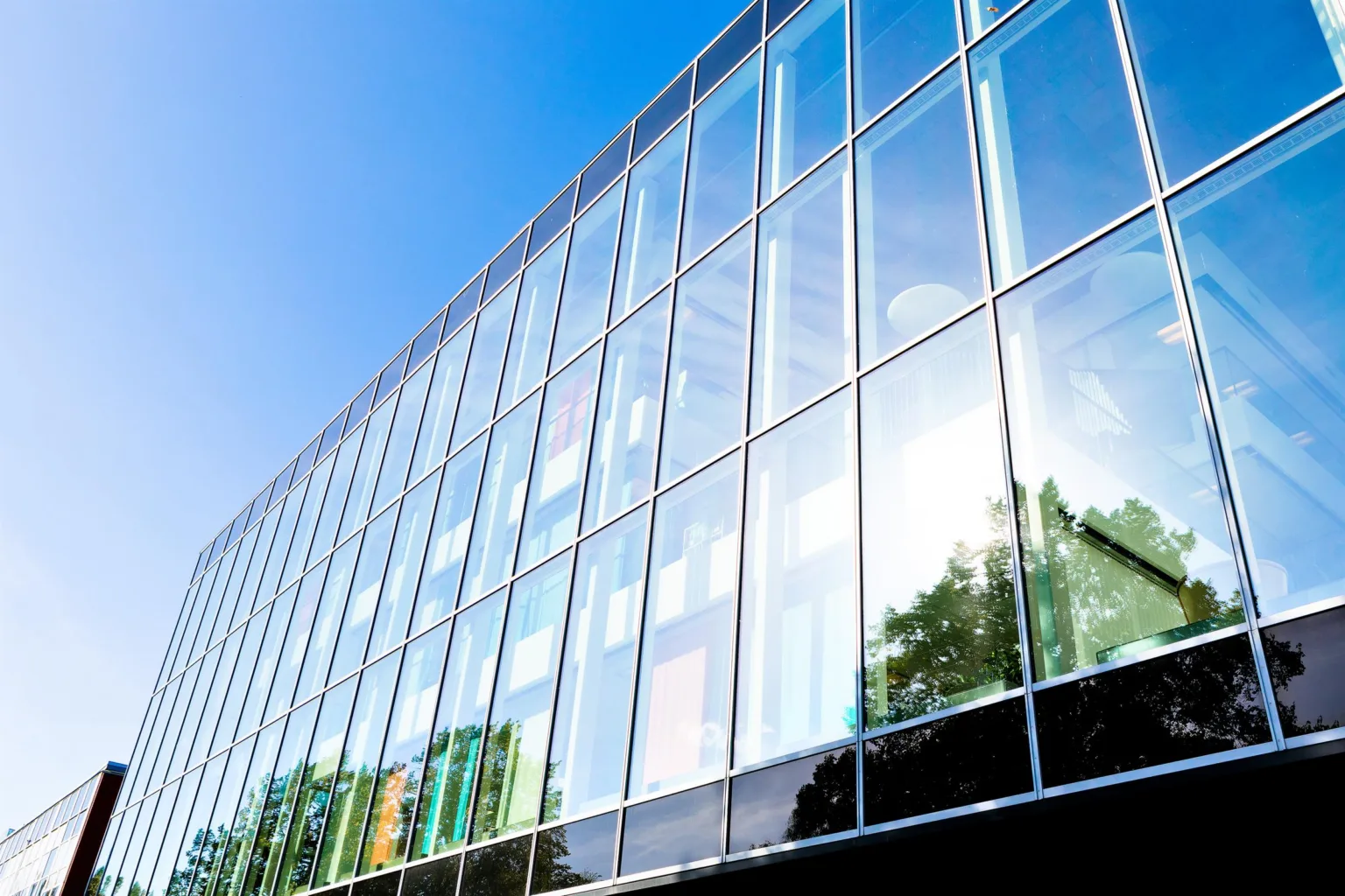 En modern byggnad med glasfasad som reflekterar blå himmel och träd.