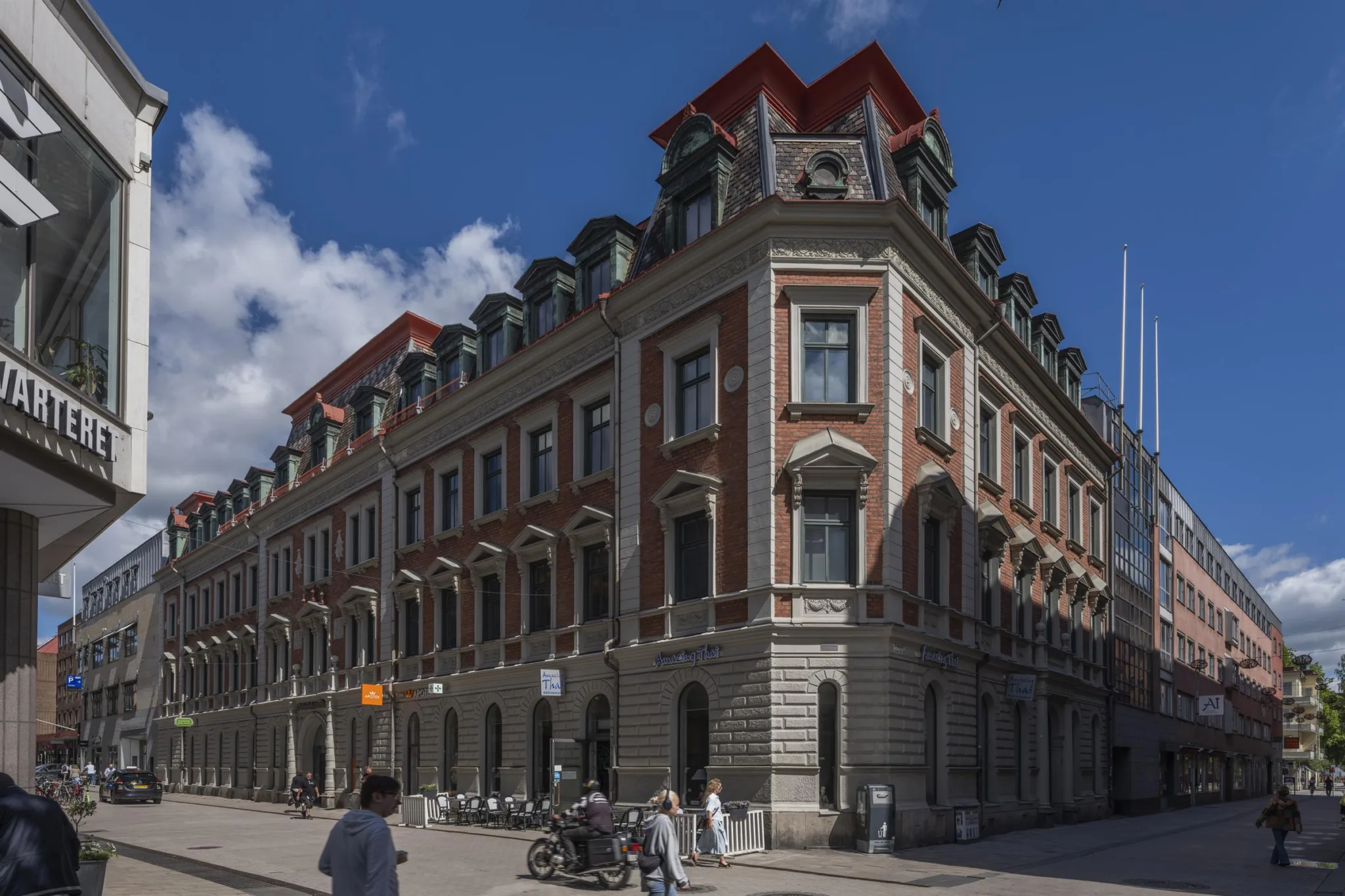 1. En klassisk byggnad med röd takkupol och detaljerad fasad, människor går på trottoaren under en blå himmel.