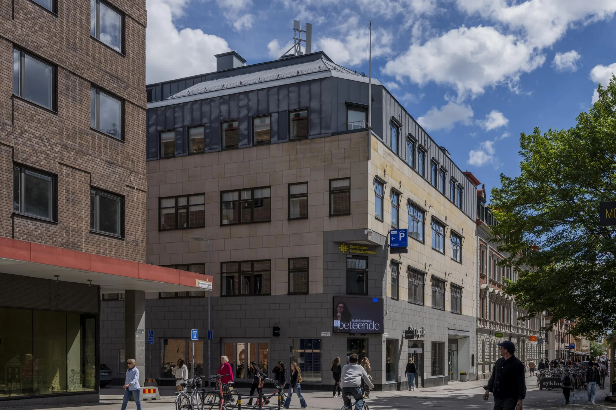 4. En modern byggnad med glasdetaljer och en busshållplats framför, flera människor går längs gatan.