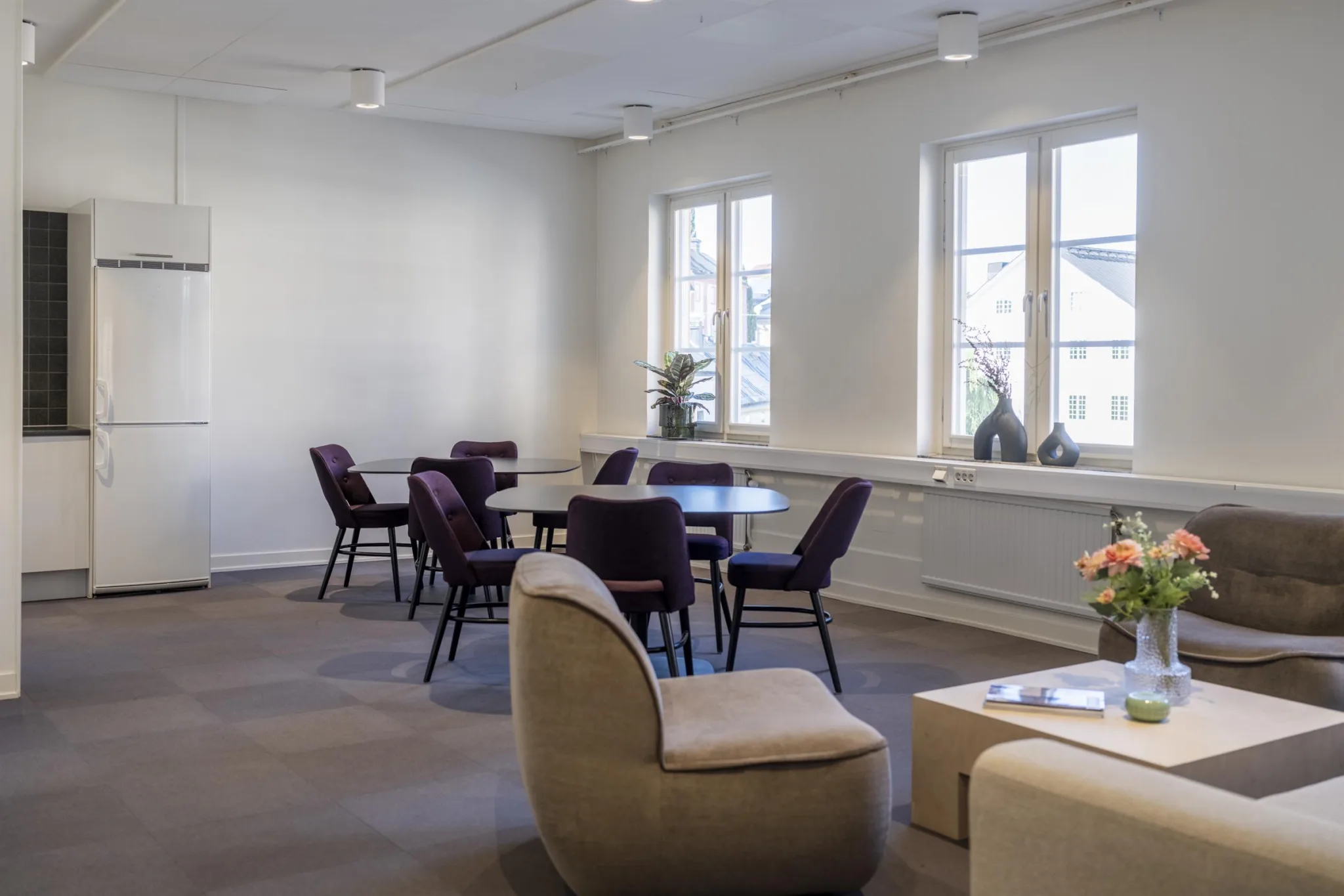 3. Ett loungeområde med runda bord, lila stolar och beige fåtöljer nära fönster.