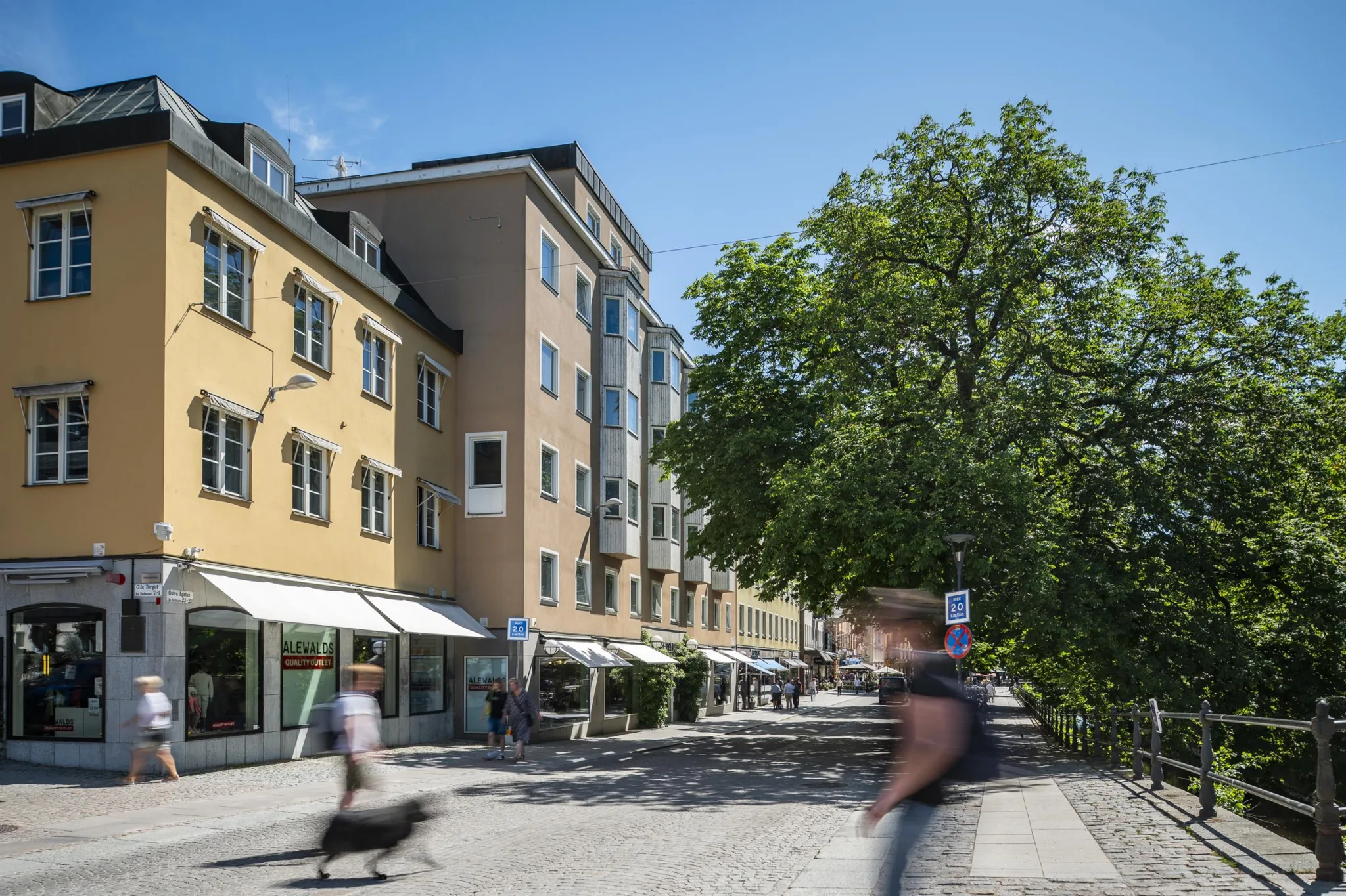 4. Gata med gula byggnader, ett träd och människor som passerar.