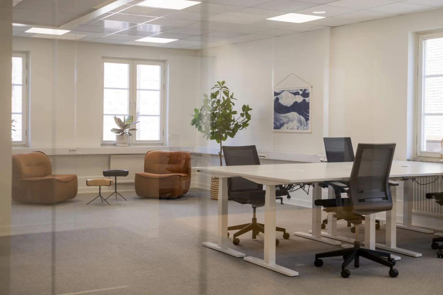 1. Ett modernt kontor med skrivbord, kontorsstolar, växter och konst på väggen.