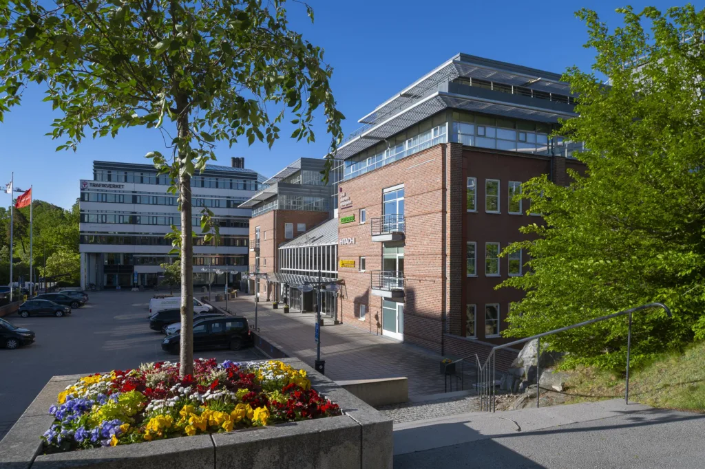 5. En modern byggnad med tegel- och glasfasad, omgiven av träd och blommor i en planteringslåda, sett under en solig dag.