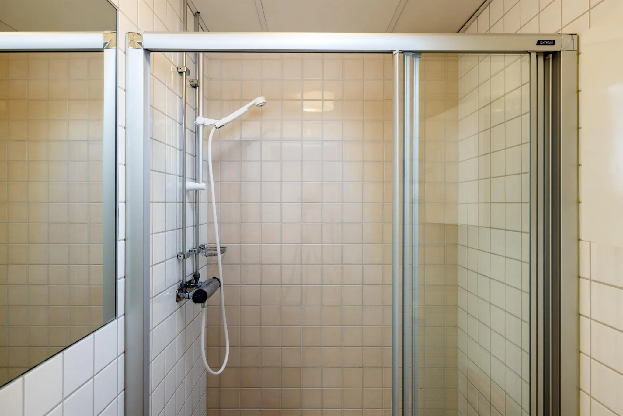 3. Ett duschområde med vita kaklade väggar, en duschmunstycke och glasdörrar.