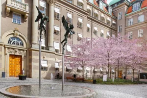 Två statyer av bevingade figurer på pelare framför en byggnad med körsbärsträd i blom.