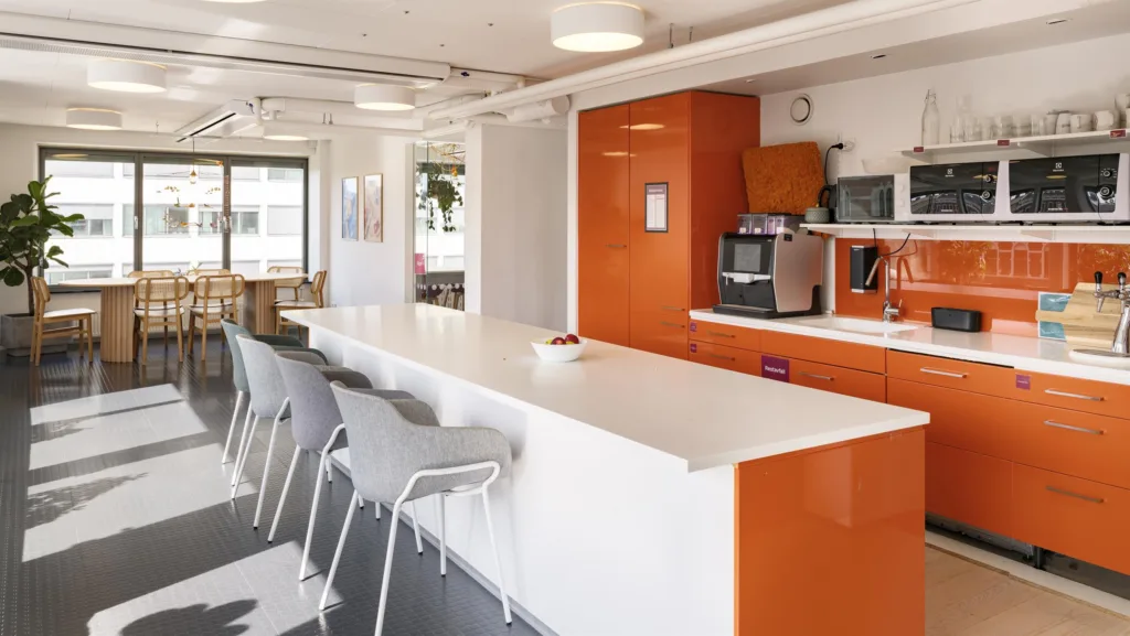 4. Ett modernt kök med en orange köksbänk, vit bardisk och flera gråa stolar.