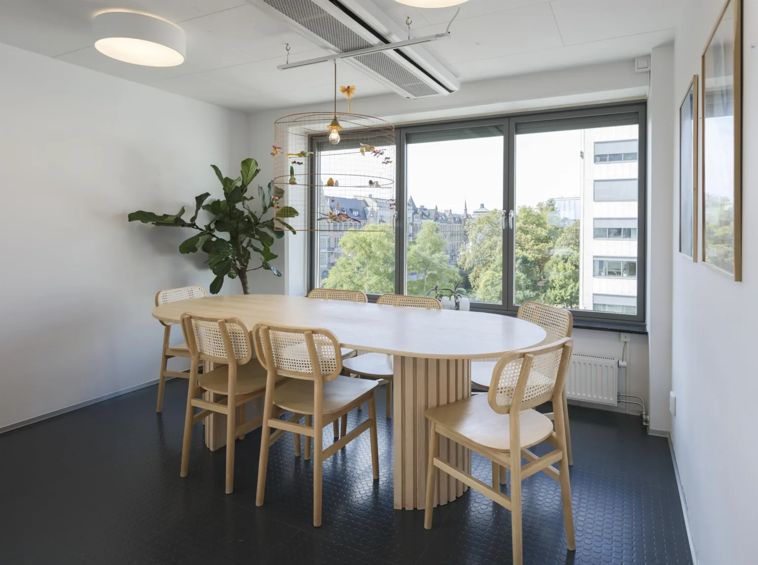 3. Ett konferensrum med ett runt bord, sex ljusa trästolar och fönster som vetter mot grönska och byggnader.