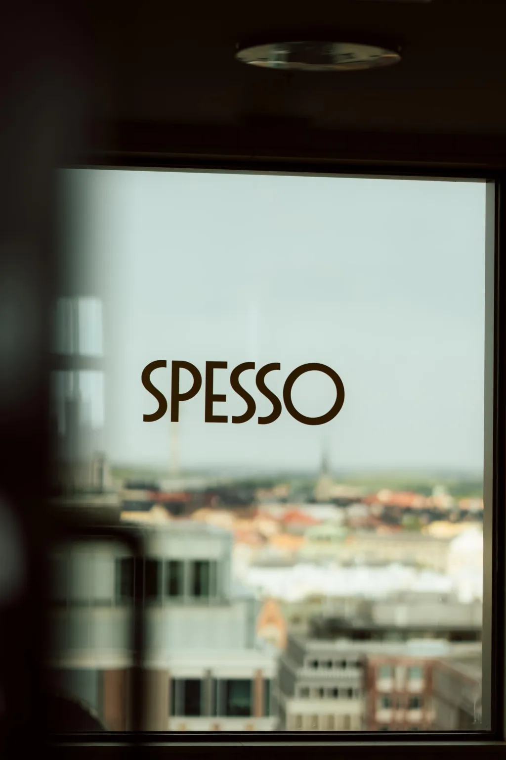 Glasfönster med texten "SPESSO", stadens silhuett i bakgrunden.