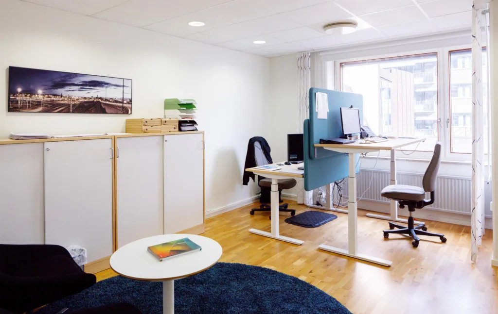 2. Ett kontorsrum med skrivbord, höj- och sänkbara arbetsstationer, skåp och ett runt soffbord.