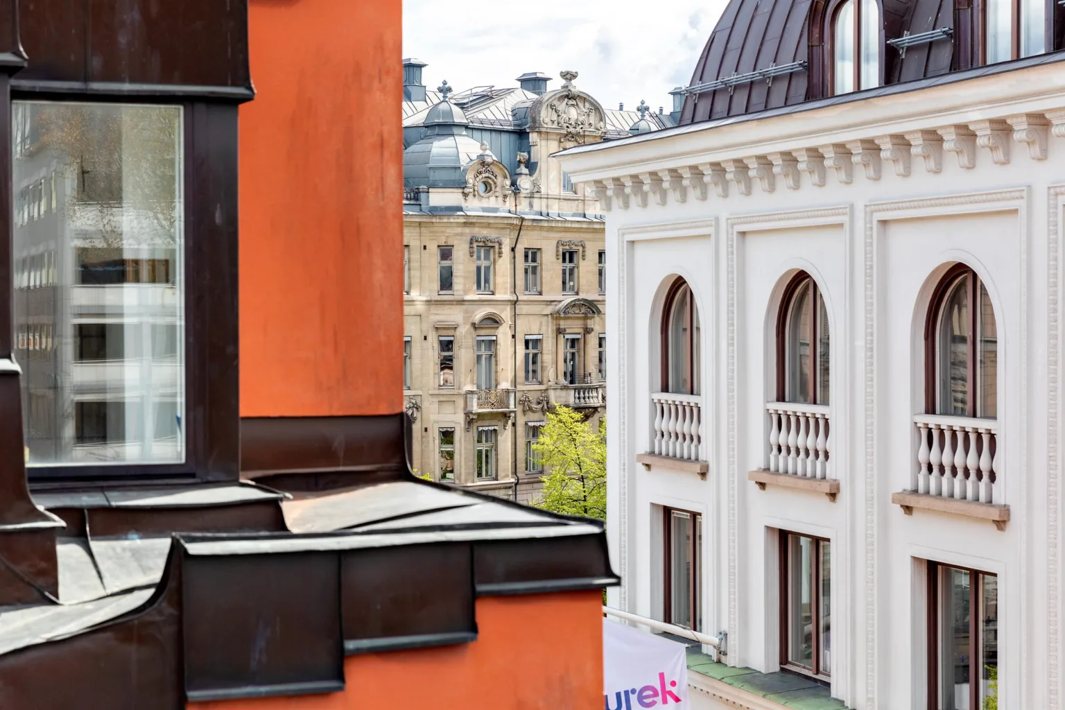 En närbild av en orange fasad med utsikt över klassiska byggnader och tak i stadsmiljö.