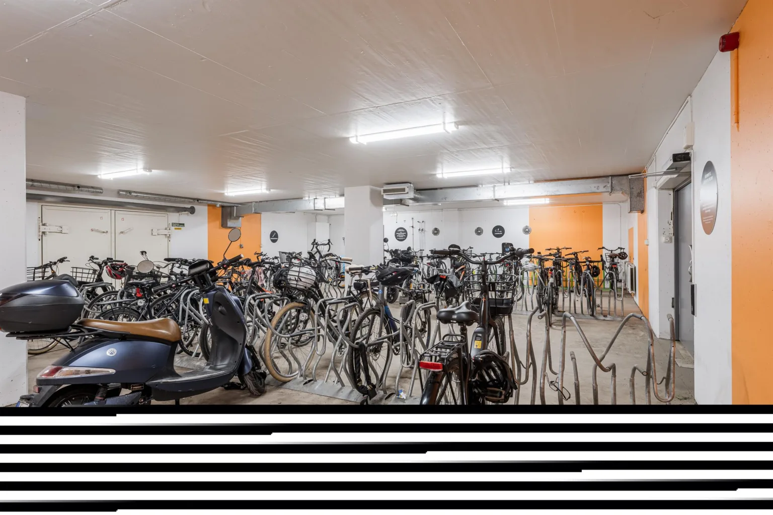 Cykelrum med flera cyklar parkerade i ställ under takbelysning.