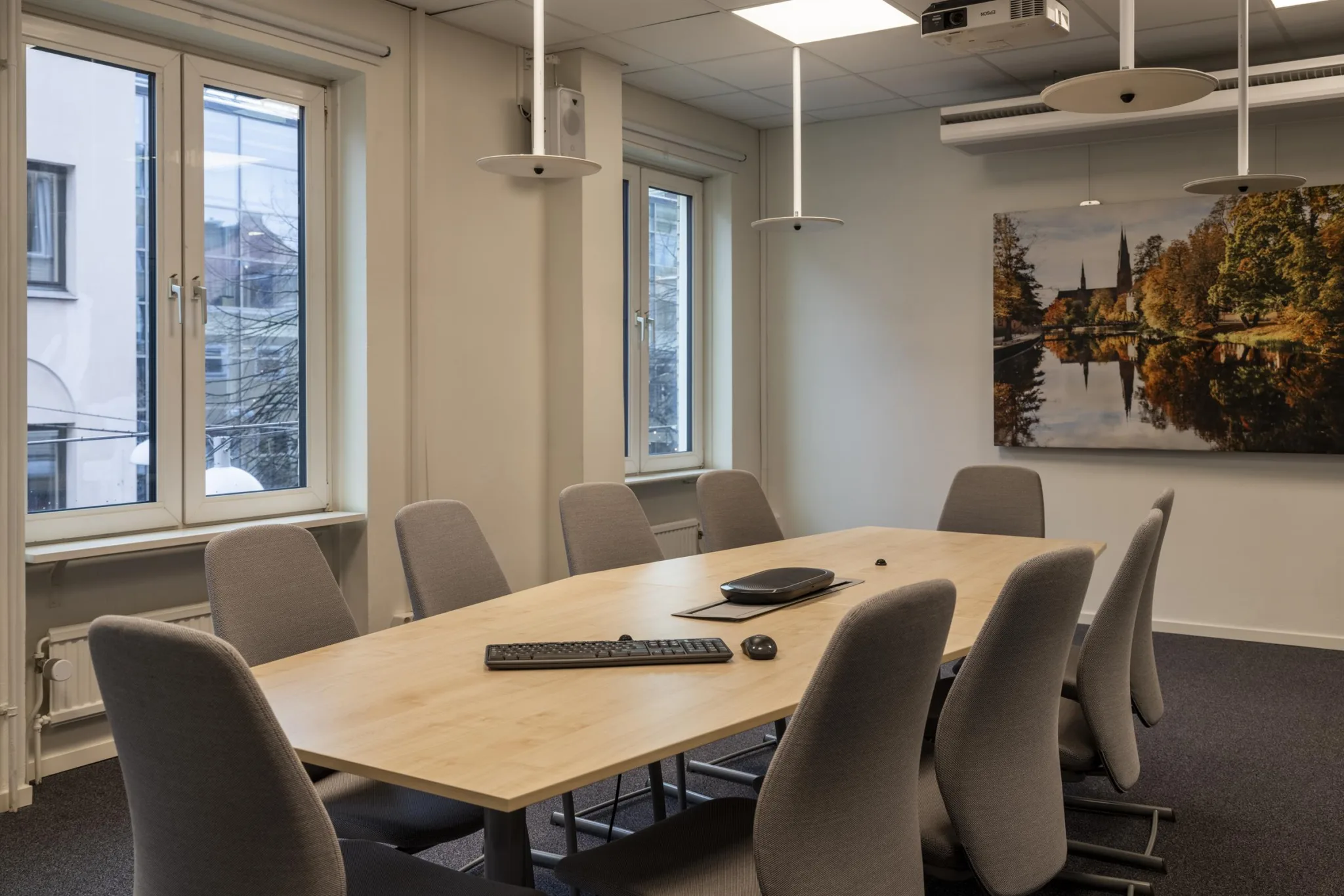 Ett konferensrum med ett stort bord, gråa stolar och fönster som släpper in naturligt ljus.