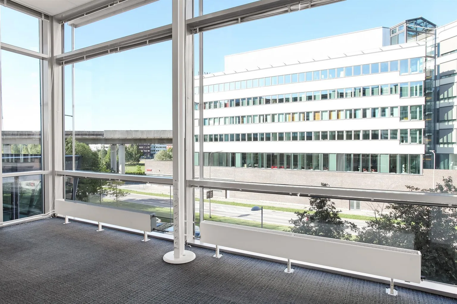 Ett stort fönster med utsikt mot en modern byggnad och grönområden utanför.