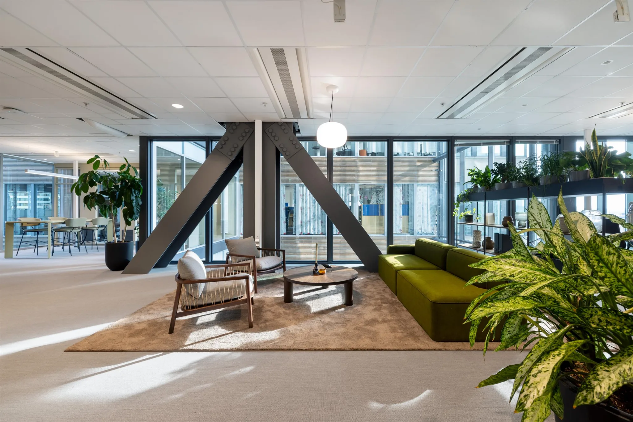 En stilfull lounge med en grön soffa, stolar, ett soffbord och stora fönster.