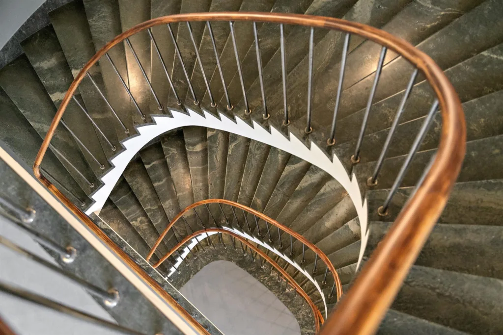 En spiraltrappa med metallräcke och steg klädda i mörk sten.