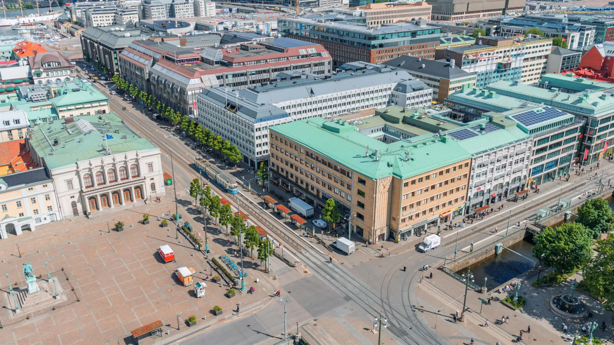 En fågelperspektiv över ett torg med byggnader, träd och trafik i en stadsmiljö.