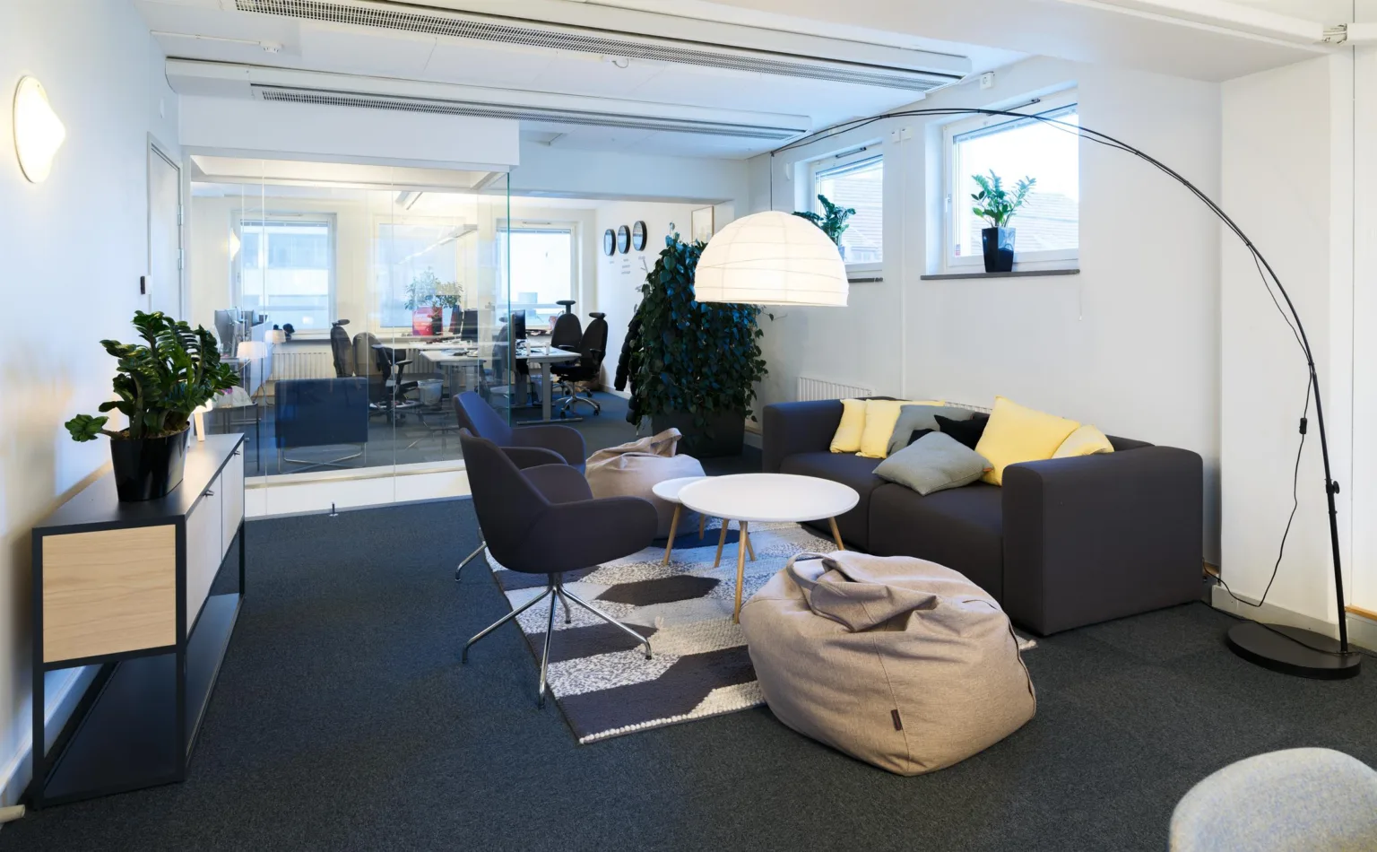 2. En sittgrupp med soffa, fåtöljer, en sittsäck, soffbord och en stor lampa i ett kontor med glasväggar.