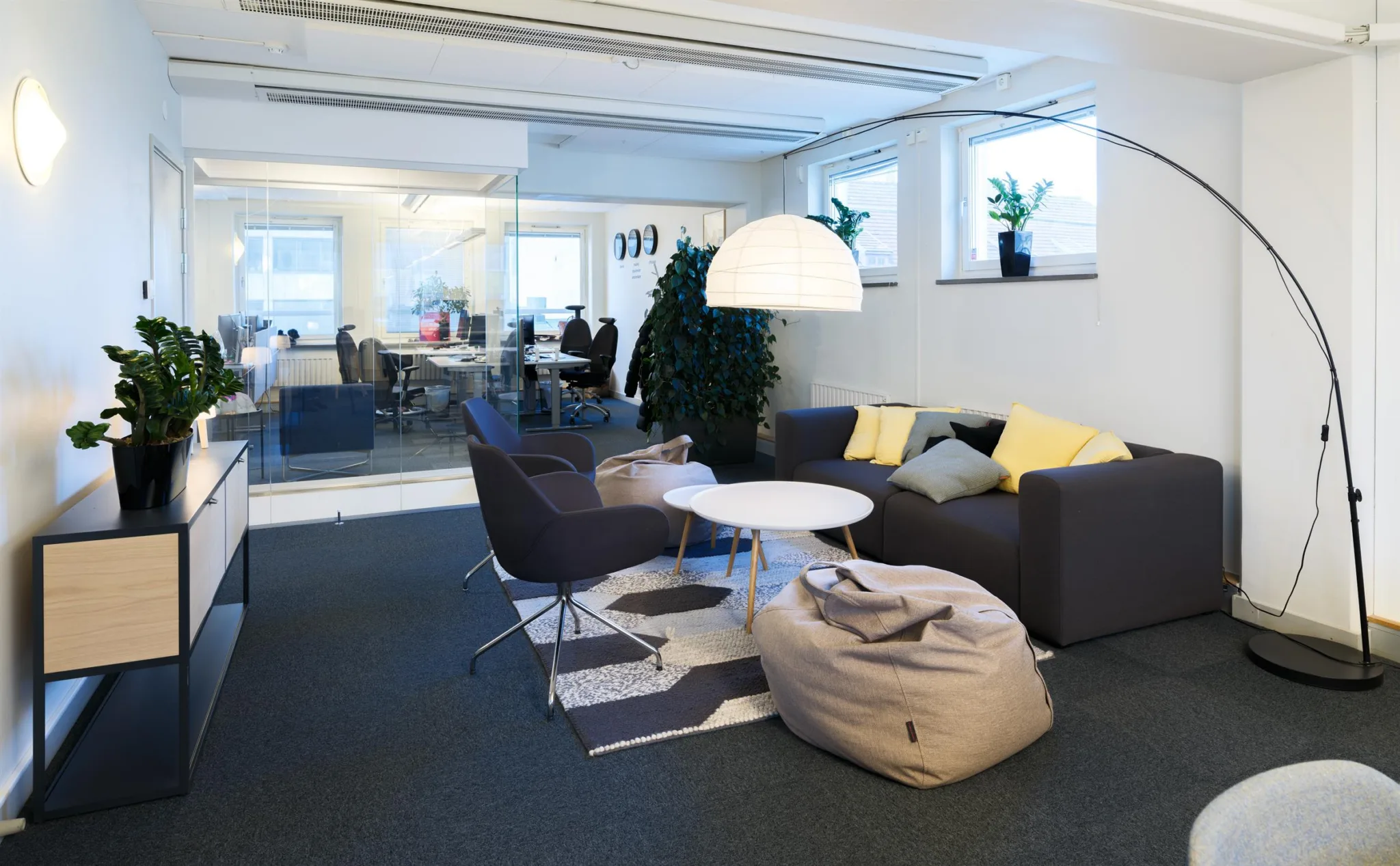 2. En sittgrupp med soffa, fåtöljer, en sittsäck, soffbord och en stor lampa i ett kontor med glasväggar.