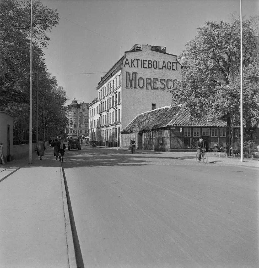 En svartvit bild av en gata med en stor byggnad med texten "Arbetarbladet Moresco" på fasaden.