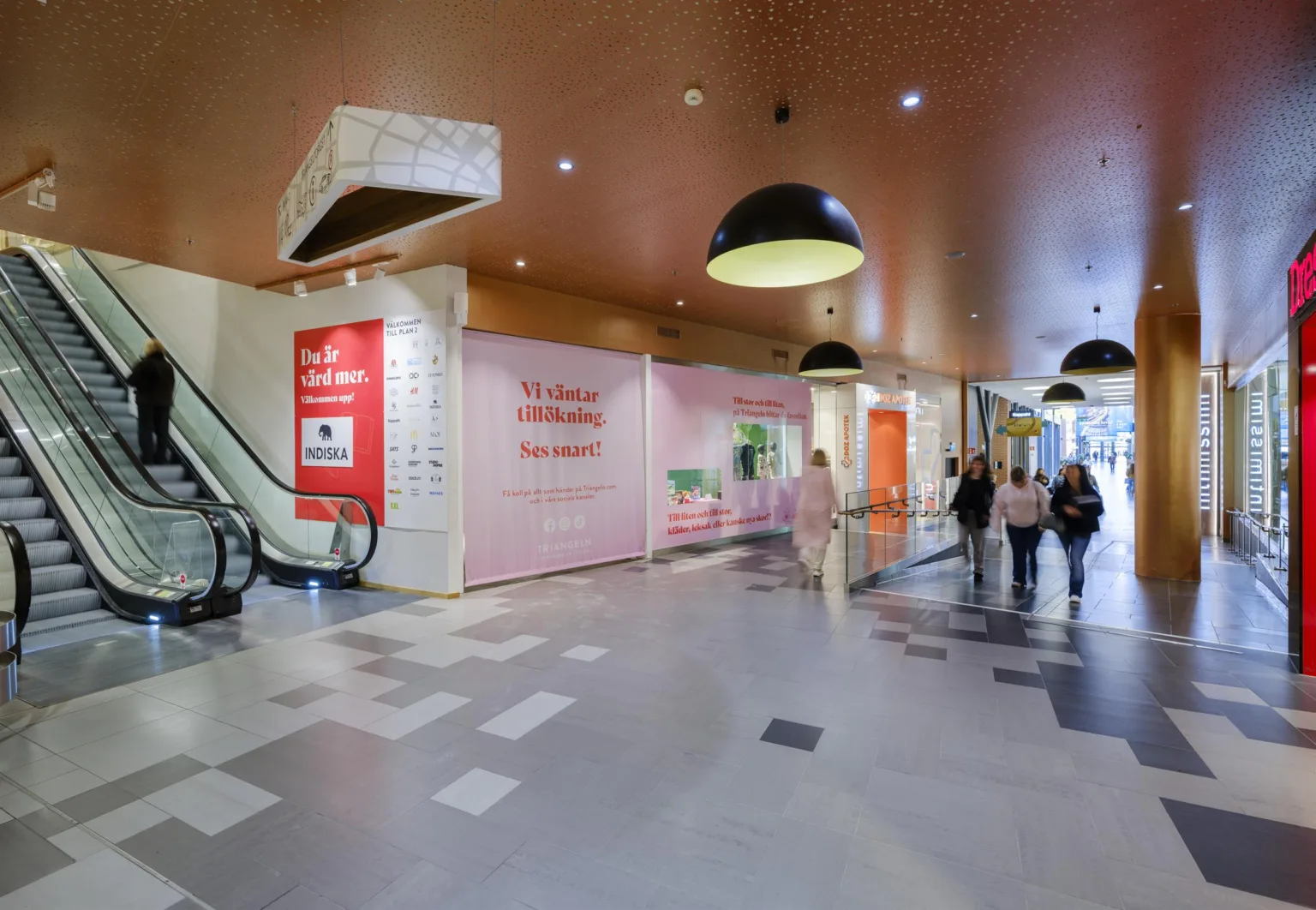 2. En köpcentrumgång med rosa väggar, röda reklamskyltar och några personer som går förbi.