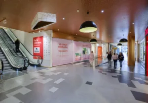 2. En köpcentrumgång med rosa väggar, röda reklamskyltar och några personer som går förbi.