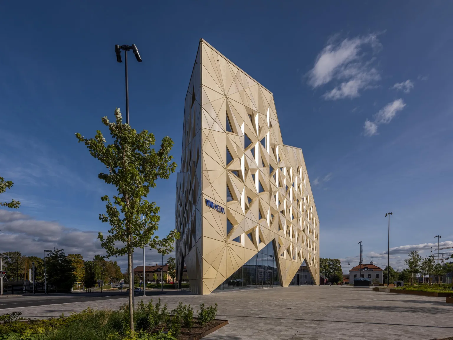 En modern arkitektonisk byggnad med triangulära detaljer och en omgivning med träd och öppna ytor.