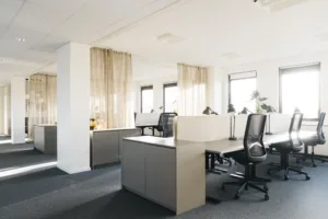 En kontorsmiljö med arbetsstationer, stolar och gardiner som delar upp utrymmet.