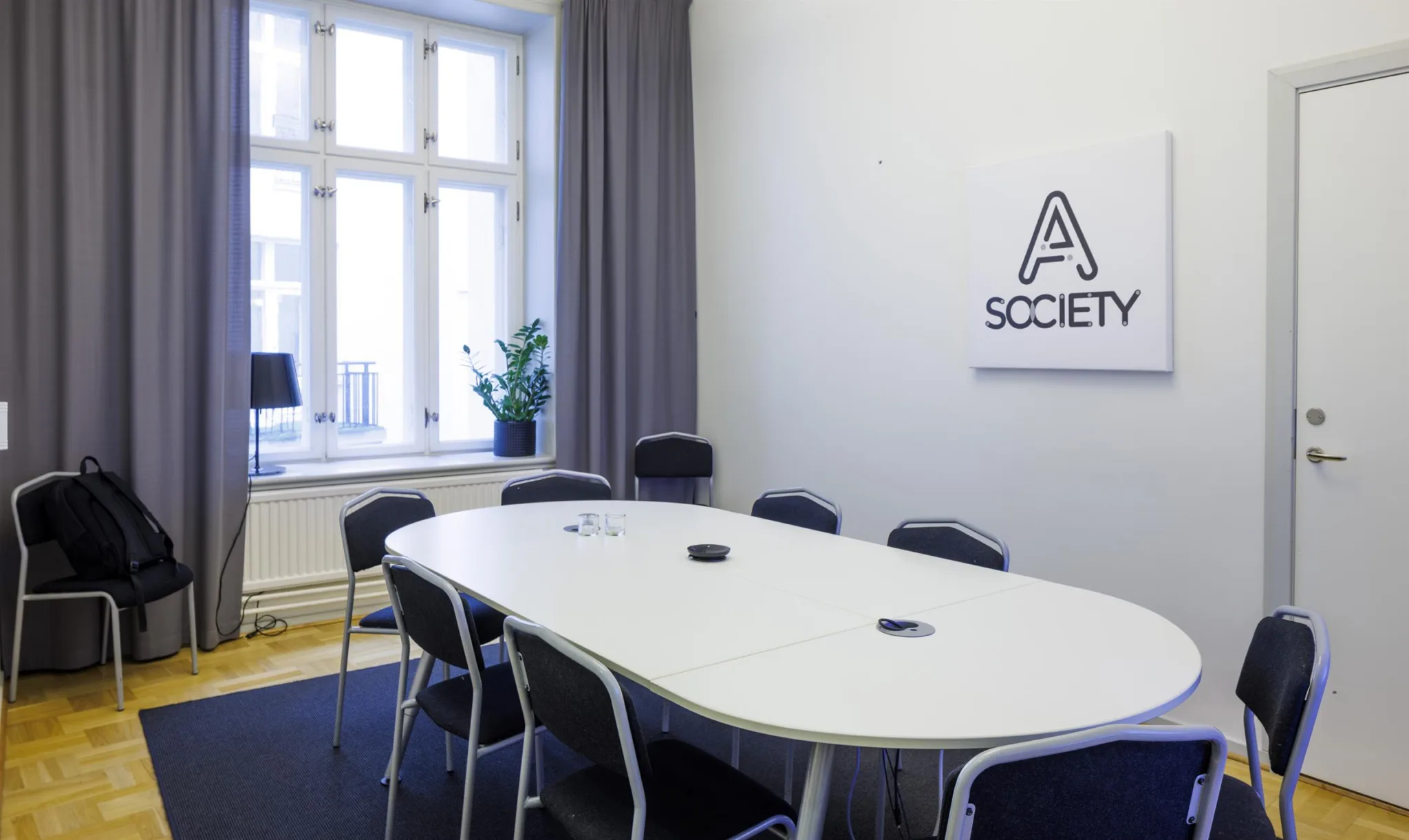 2. Ett konferensrum med ett ovalt vitt bord omgivet av svarta stolar och en vägg med texten "A Society".