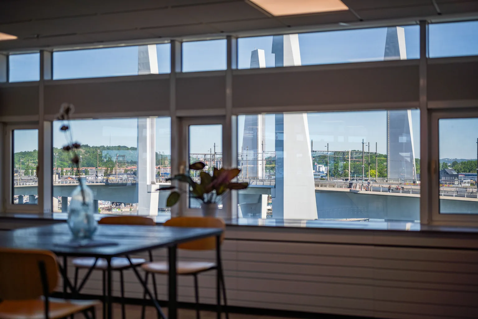 3. Utsikt över en bro och vatten från ett rum med stora fönster och en hög barbord med stolar.