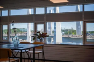 3. Utsikt över en bro och vatten från ett rum med stora fönster och en hög barbord med stolar.