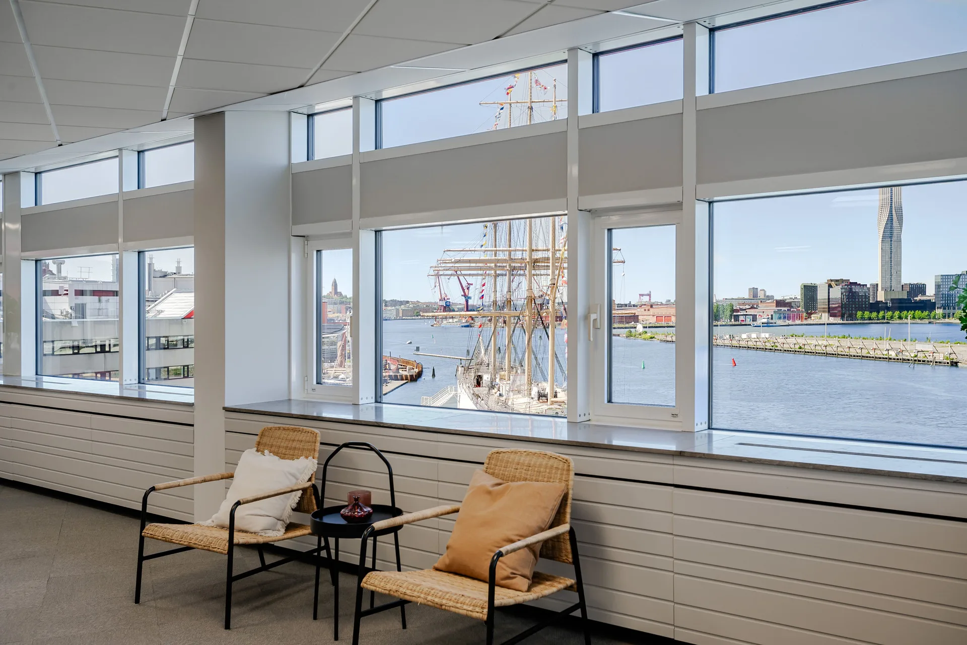 4. Två fåtöljer och ett litet bord placerade framför stora fönster med utsikt över en hamn och segelbåtar.