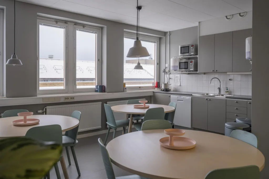3. Ett ljust kök med flera runda bord, stolar och köksutrustning.