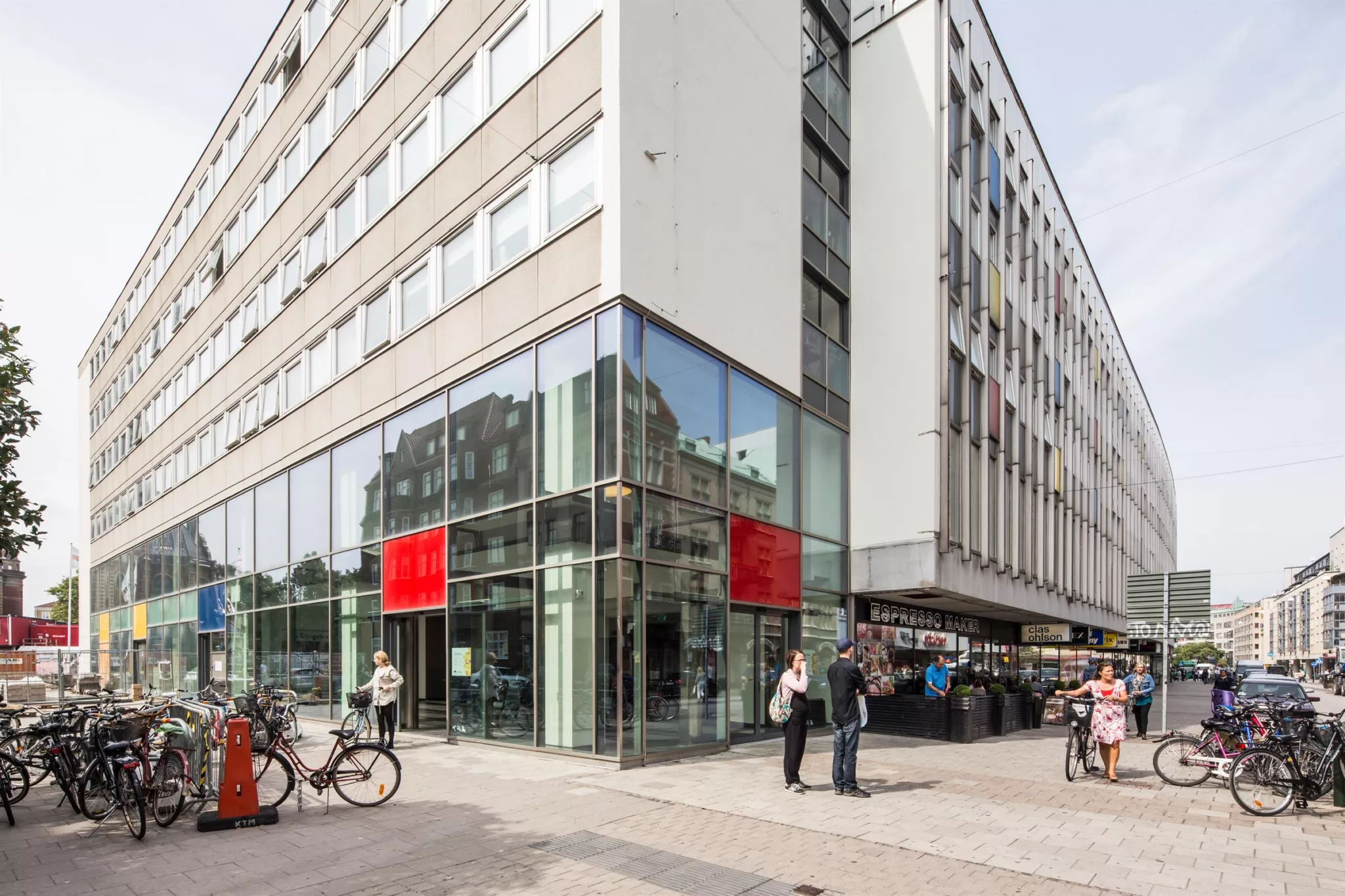 4. En hörnbyggnad med glasfönster, röda skyltar och människor som går förbi.