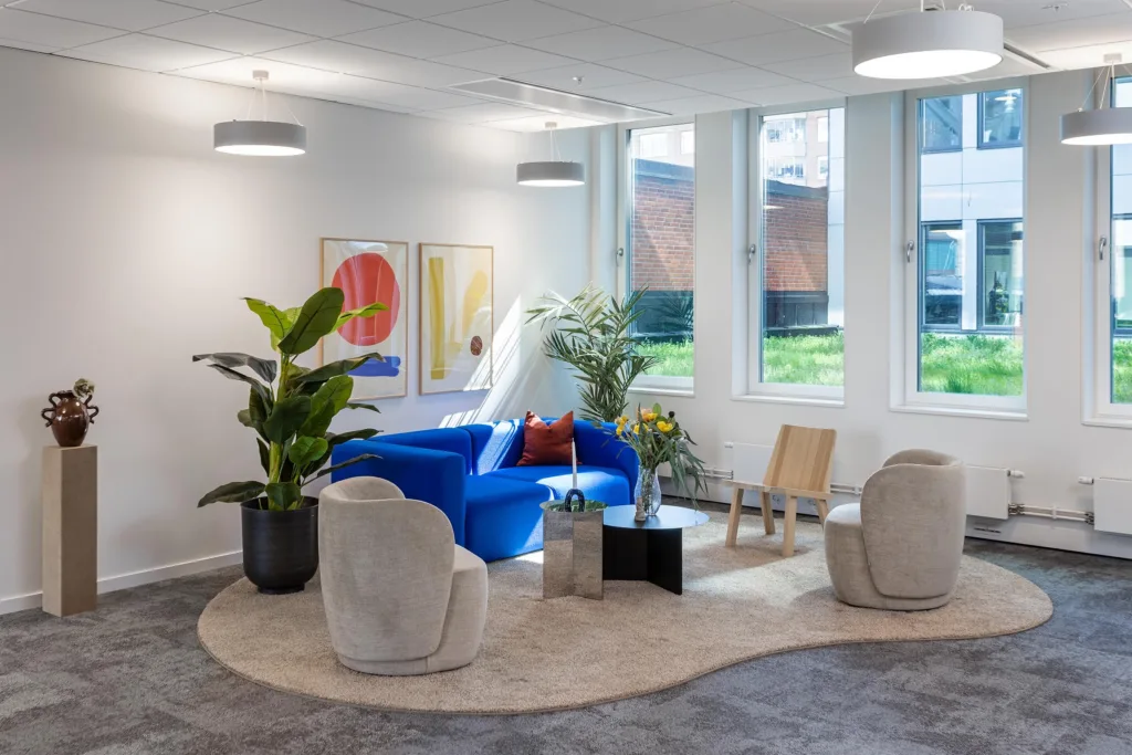En ljus och modern lounge med blå soffa, vita fåtöljer, växter och konstverk på väggarna.