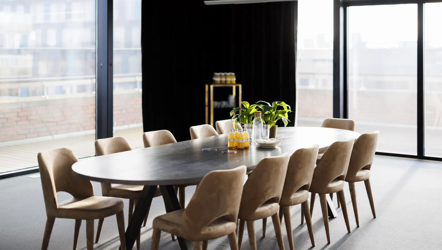 Ett elegant mötesrum med ett långt mörkt bord, omgiven av beige stolar och dekorerat med gröna växter och glasflaskor.