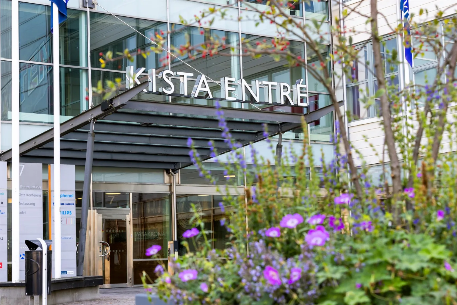 Entrén till Kista Entré med blommor i förgrunden och glasfasad i bakgrunden.