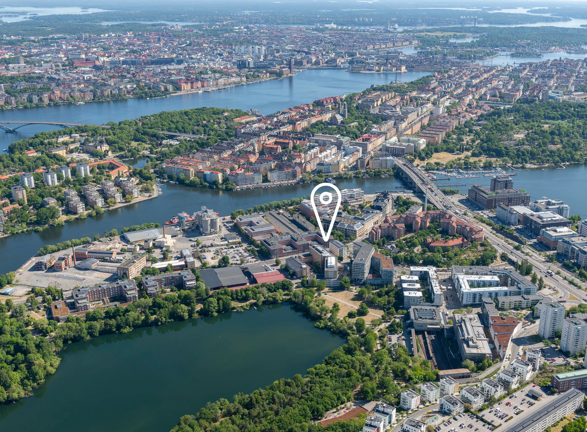 5. Flygfoto över en stad med grönområden, vatten och byggnader, med en markör som indikerar en plats.