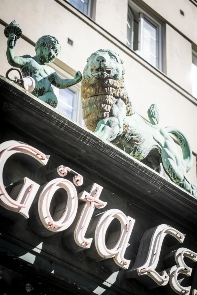 5. En skylt med texten "Göta" i neon ovanför en entré, dekorerad med gröna skulpturer av lejon och figurer.