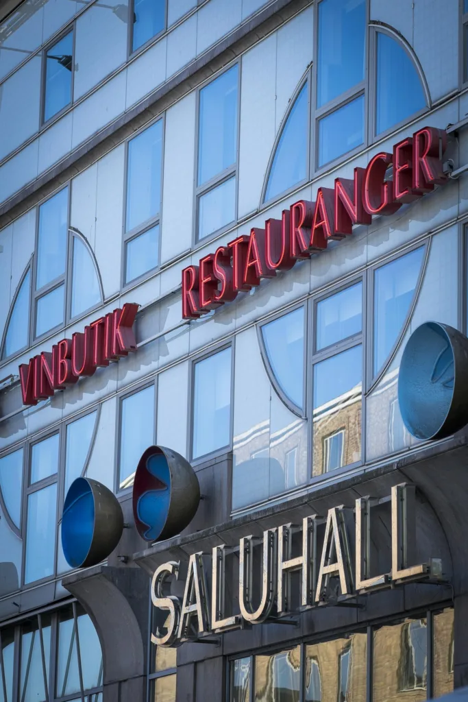 Närbild på en byggnad med skyltar som lyder "VINSBUTIK" och "RESTAURANGER" ovanför texten "SALUHALL".