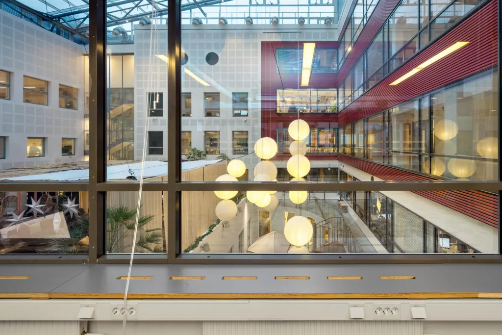 Ett inomhusutrymme sett genom ett stort fönster, med runda hängande lampor och en modern interiördesign.