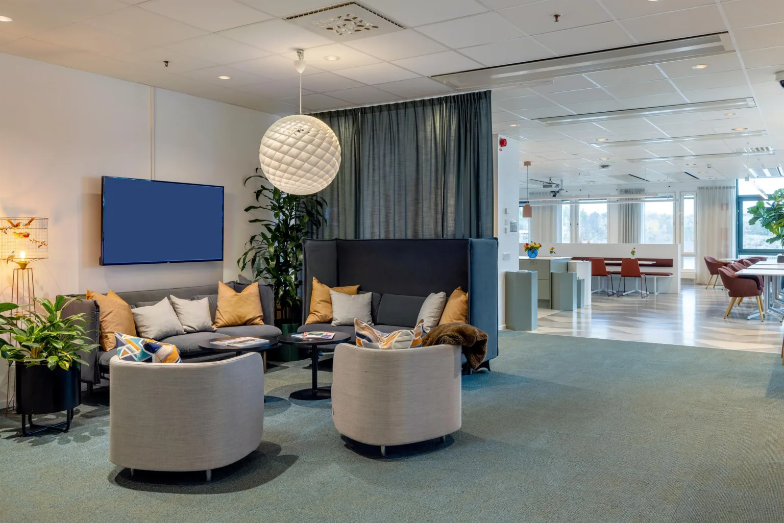 3. En lounge med soffgrupp, fåtöljer, kuddar, en rund lampa och växter.