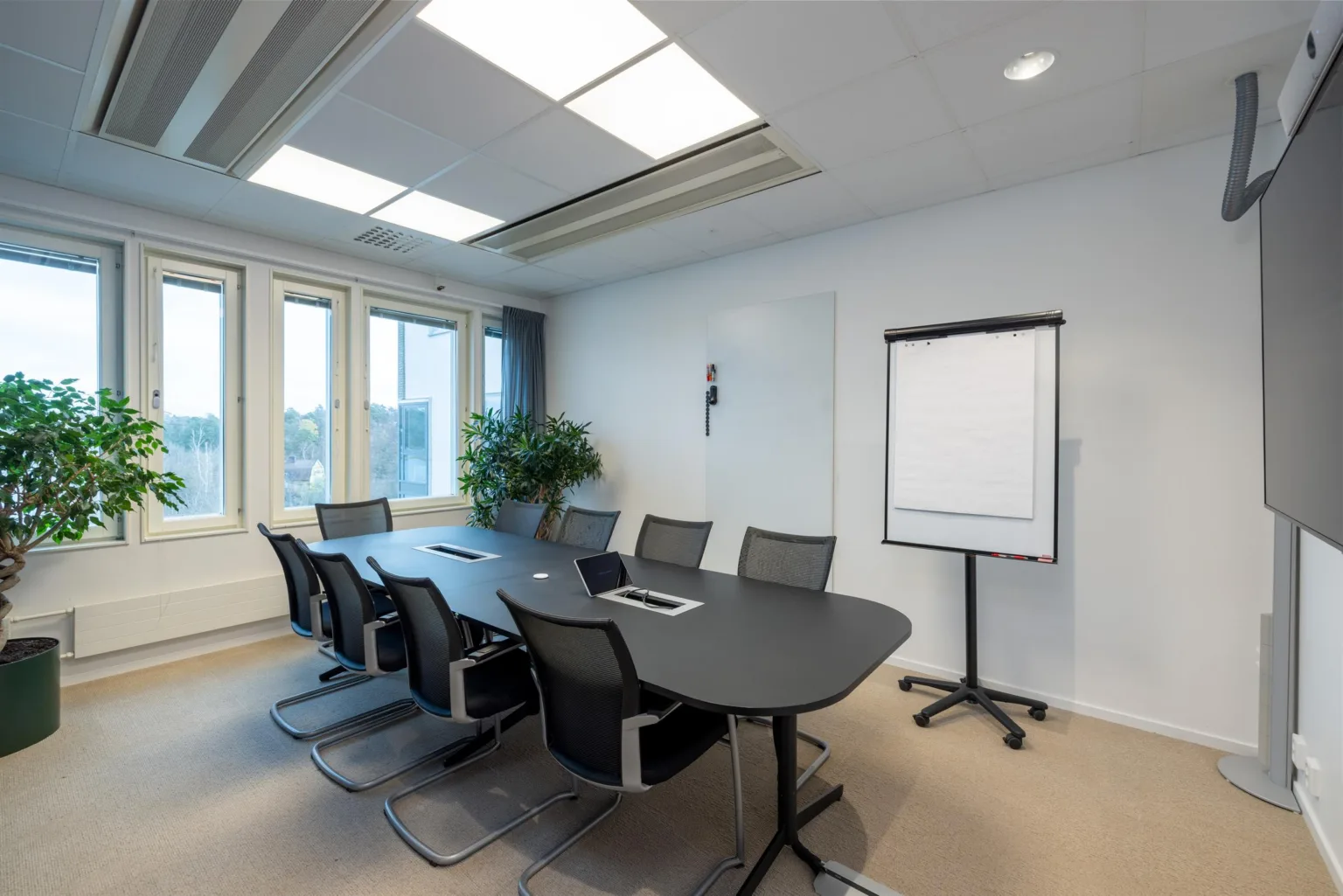 3. Ett konferensrum med ett ovalt bord, flera stolar, en whiteboard och ett fönster med utsikt.